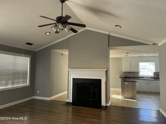 unfurnished living room with sink, wood-type flooring, lofted ceiling, a textured ceiling, and ornamental molding