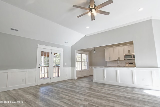 unfurnished living room with french doors, vaulted ceiling, ceiling fan, ornamental molding, and light hardwood / wood-style floors