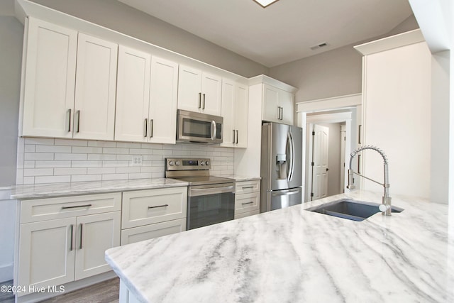 kitchen with light stone countertops, white cabinetry, sink, and appliances with stainless steel finishes