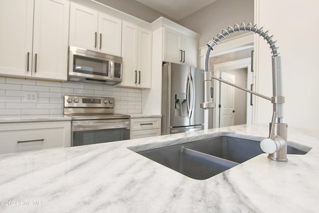 kitchen with white cabinets, sink, decorative backsplash, light stone counters, and stainless steel appliances