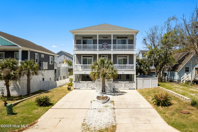 coastal inspired home with concrete driveway, a front lawn, and a balcony