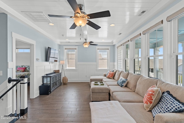 living room featuring dark wood-style floors, visible vents, a wainscoted wall, and a ceiling fan