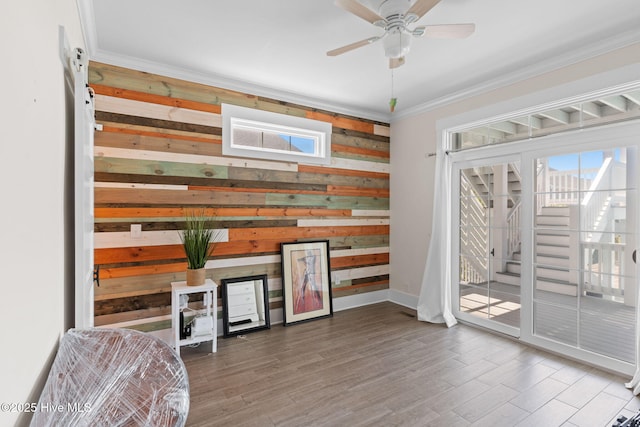 living area with ornamental molding, ceiling fan, wood walls, and wood finished floors