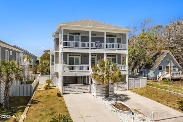 beach home with a front yard, a balcony, covered porch, concrete driveway, and fence