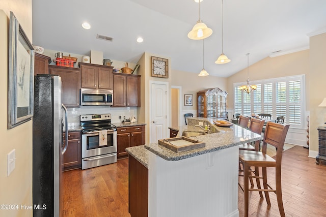 kitchen featuring dark hardwood / wood-style flooring, an island with sink, pendant lighting, a breakfast bar, and appliances with stainless steel finishes