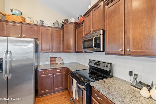 kitchen with vaulted ceiling, decorative backsplash, light hardwood / wood-style floors, light stone counters, and stainless steel appliances