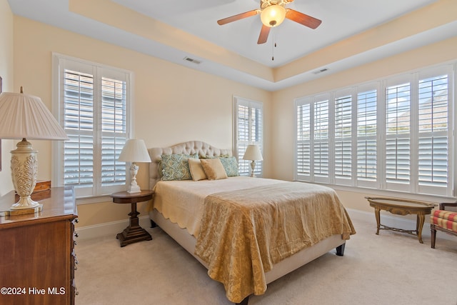 bedroom featuring light colored carpet, a raised ceiling, multiple windows, and ceiling fan