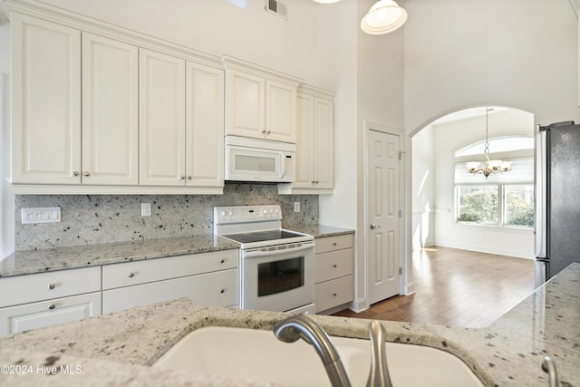 kitchen with a towering ceiling, dark hardwood / wood-style flooring, light stone counters, white appliances, and decorative light fixtures