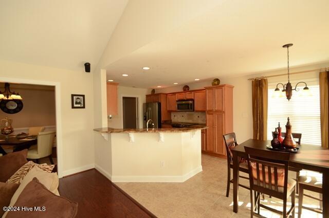 kitchen with kitchen peninsula, appliances with stainless steel finishes, pendant lighting, a chandelier, and a breakfast bar area