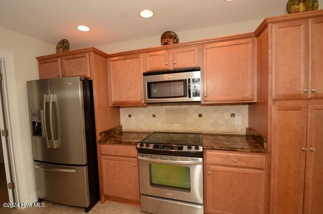 kitchen featuring light tile patterned floors, backsplash, appliances with stainless steel finishes, and dark stone counters