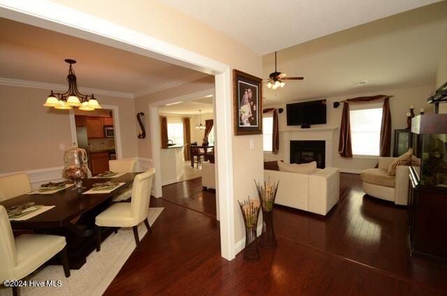 dining space featuring dark wood-type flooring, ceiling fan with notable chandelier, and ornamental molding