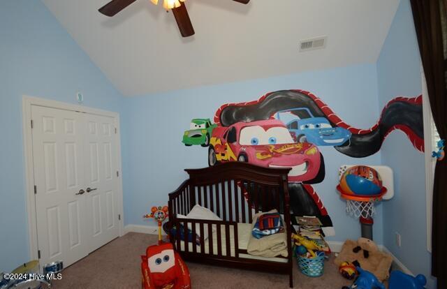 carpeted bedroom with ceiling fan, a nursery area, and vaulted ceiling