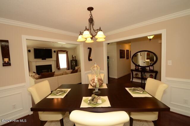 dining space with crown molding, dark wood-type flooring, and an inviting chandelier