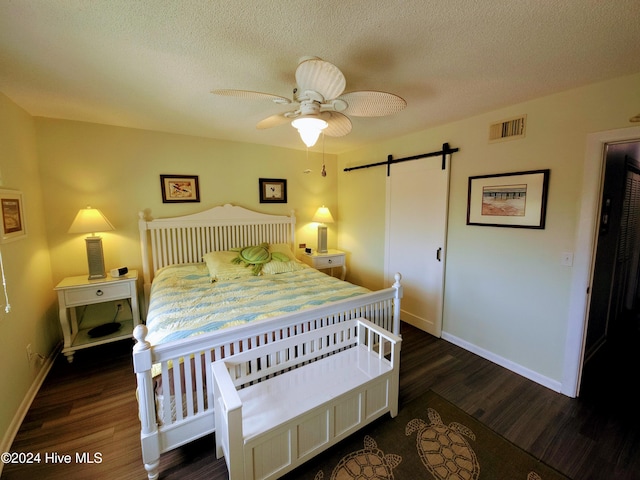 bedroom featuring a textured ceiling, dark hardwood / wood-style flooring, ceiling fan, and a barn door