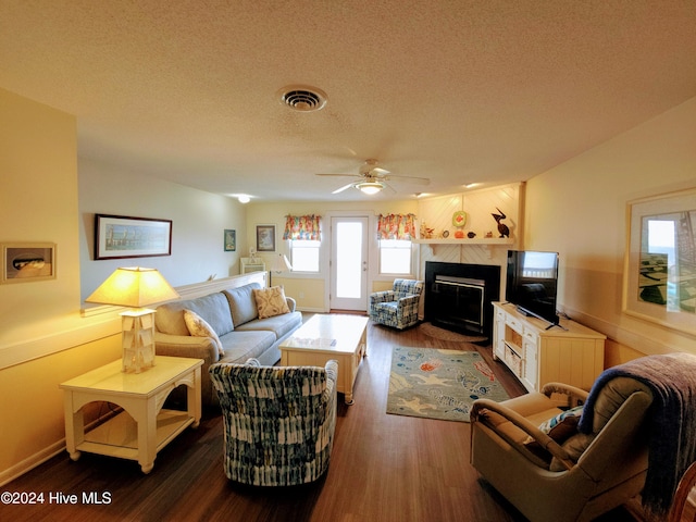 living room with ceiling fan, dark hardwood / wood-style flooring, a textured ceiling, and a tiled fireplace