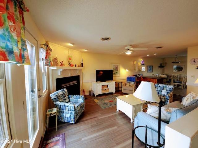 living room with ceiling fan, a fireplace, wood-type flooring, and a textured ceiling