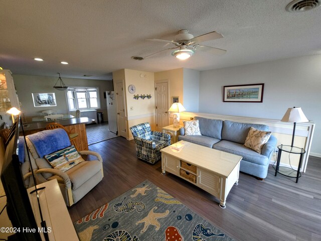 living room featuring ceiling fan, dark hardwood / wood-style flooring, and a textured ceiling