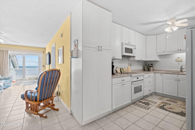 kitchen featuring white cabinets, light tile patterned flooring, white appliances, and a textured ceiling