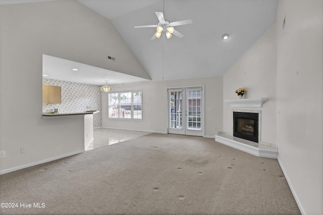 unfurnished living room with ceiling fan with notable chandelier, light colored carpet, and high vaulted ceiling