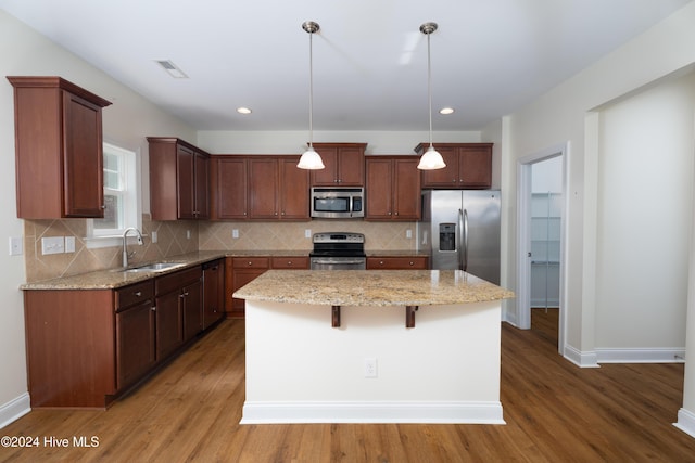 kitchen with appliances with stainless steel finishes, a center island, dark wood-type flooring, and pendant lighting