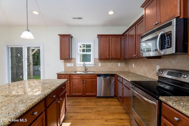 kitchen featuring light stone countertops, sink, light hardwood / wood-style flooring, decorative light fixtures, and appliances with stainless steel finishes