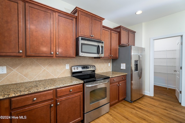 kitchen featuring backsplash, light stone countertops, light wood-type flooring, and stainless steel appliances