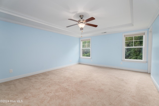 empty room featuring a tray ceiling, ceiling fan, ornamental molding, and light colored carpet