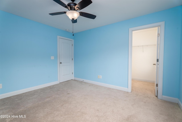 unfurnished bedroom featuring ceiling fan, a walk in closet, light carpet, and a closet