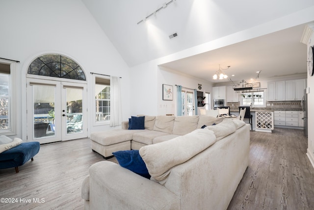 living room with high vaulted ceiling, track lighting, french doors, hardwood / wood-style flooring, and a notable chandelier