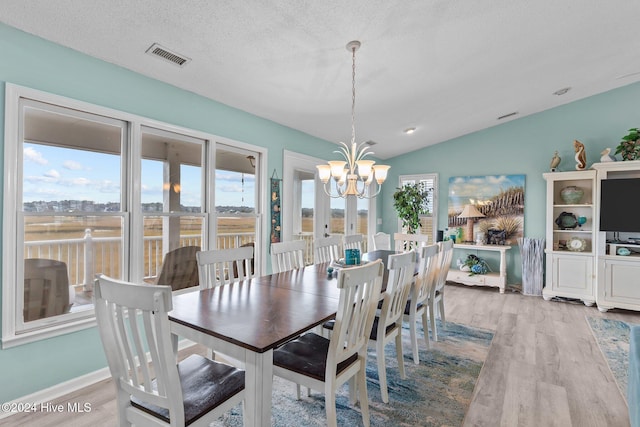 dining space featuring lofted ceiling, light hardwood / wood-style floors, a textured ceiling, and a notable chandelier