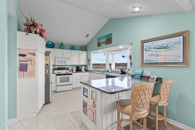 kitchen with kitchen peninsula, white appliances, a breakfast bar area, white cabinets, and lofted ceiling