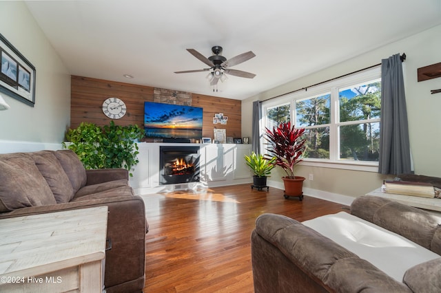 living room featuring wood-type flooring, ceiling fan, and wooden walls