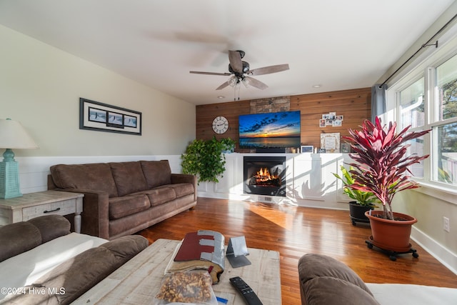 living room featuring a fireplace, light hardwood / wood-style flooring, ceiling fan, and wooden walls