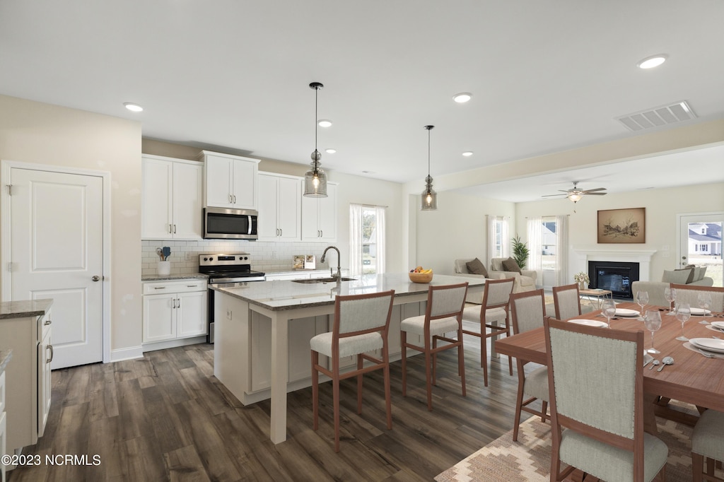 kitchen featuring a kitchen island with sink, light stone counters, white cabinets, and stainless steel appliances