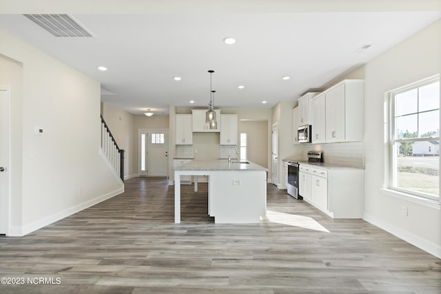 kitchen featuring a kitchen island with sink, hanging light fixtures, tasteful backsplash, white cabinetry, and stainless steel appliances