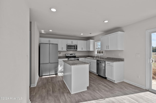 kitchen with a kitchen island, white cabinetry, light wood-type flooring, stainless steel appliances, and light stone counters