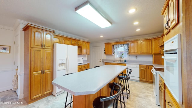 kitchen featuring a kitchen bar, white appliances, crown molding, sink, and a center island