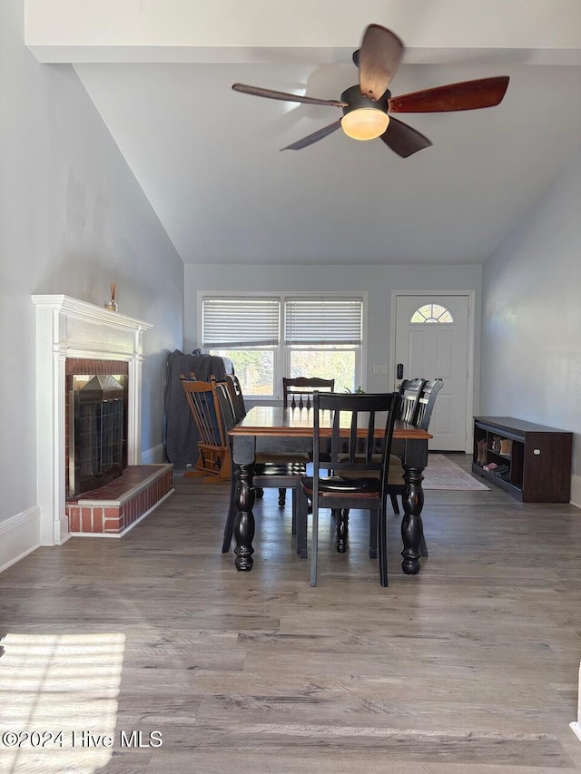 dining room featuring high vaulted ceiling, hardwood / wood-style flooring, a brick fireplace, and ceiling fan