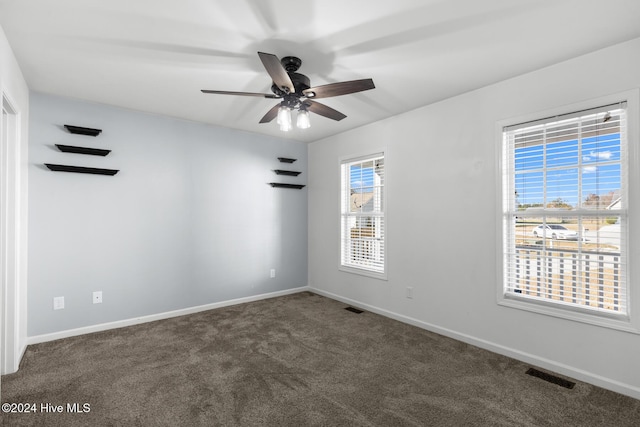 unfurnished room featuring a wealth of natural light, ceiling fan, and dark colored carpet