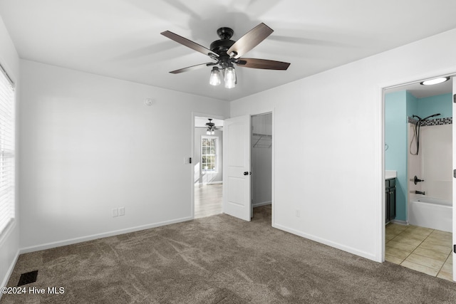 unfurnished bedroom with carpet, a walk in closet, ensuite bath, ceiling fan, and a closet