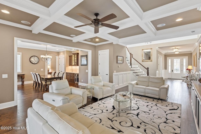 living room with beam ceiling, coffered ceiling, dark wood-type flooring, ornamental molding, and ceiling fan with notable chandelier