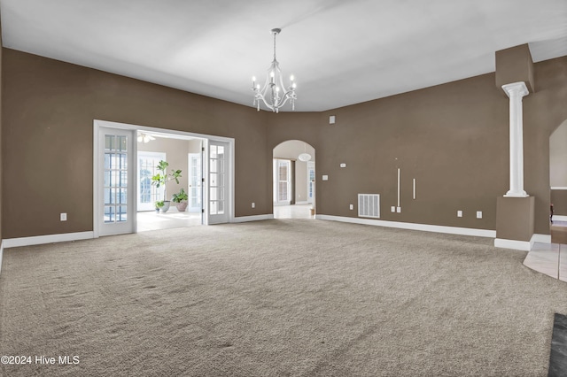 carpeted spare room with a notable chandelier, decorative columns, and french doors