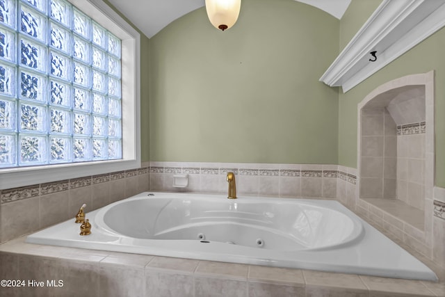 bathroom with tiled bath, vaulted ceiling, and plenty of natural light