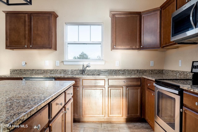 kitchen featuring appliances with stainless steel finishes, sink, light hardwood / wood-style floors, and light stone countertops