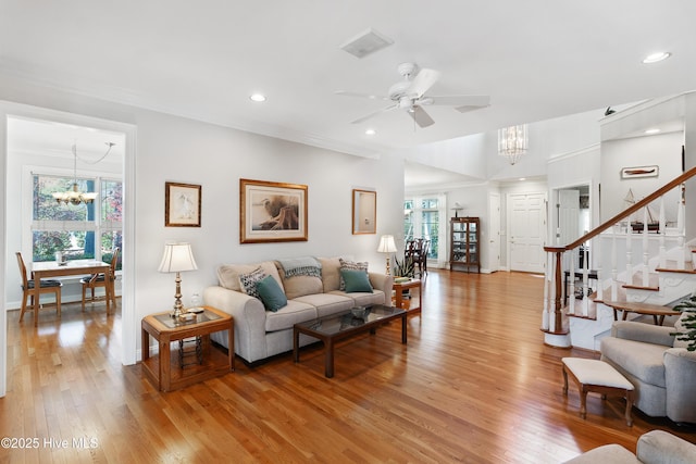 living room featuring ceiling fan with notable chandelier, wood-type flooring, and crown molding