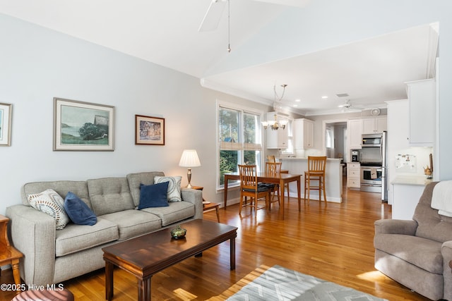 living room featuring ornamental molding, ceiling fan with notable chandelier, light hardwood / wood-style floors, and lofted ceiling