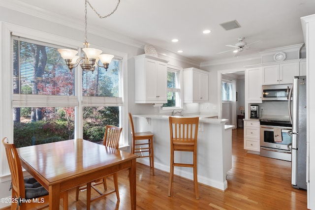 kitchen with kitchen peninsula, white cabinetry, stainless steel appliances, and ceiling fan with notable chandelier