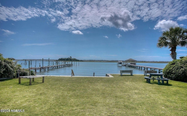 view of dock with a lawn and a water view