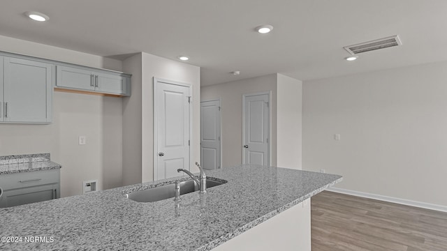 kitchen with gray cabinets, light hardwood / wood-style floors, light stone counters, and sink