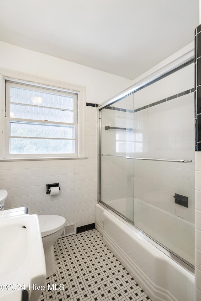 full bathroom featuring tile patterned floors, bath / shower combo with glass door, sink, tile walls, and toilet